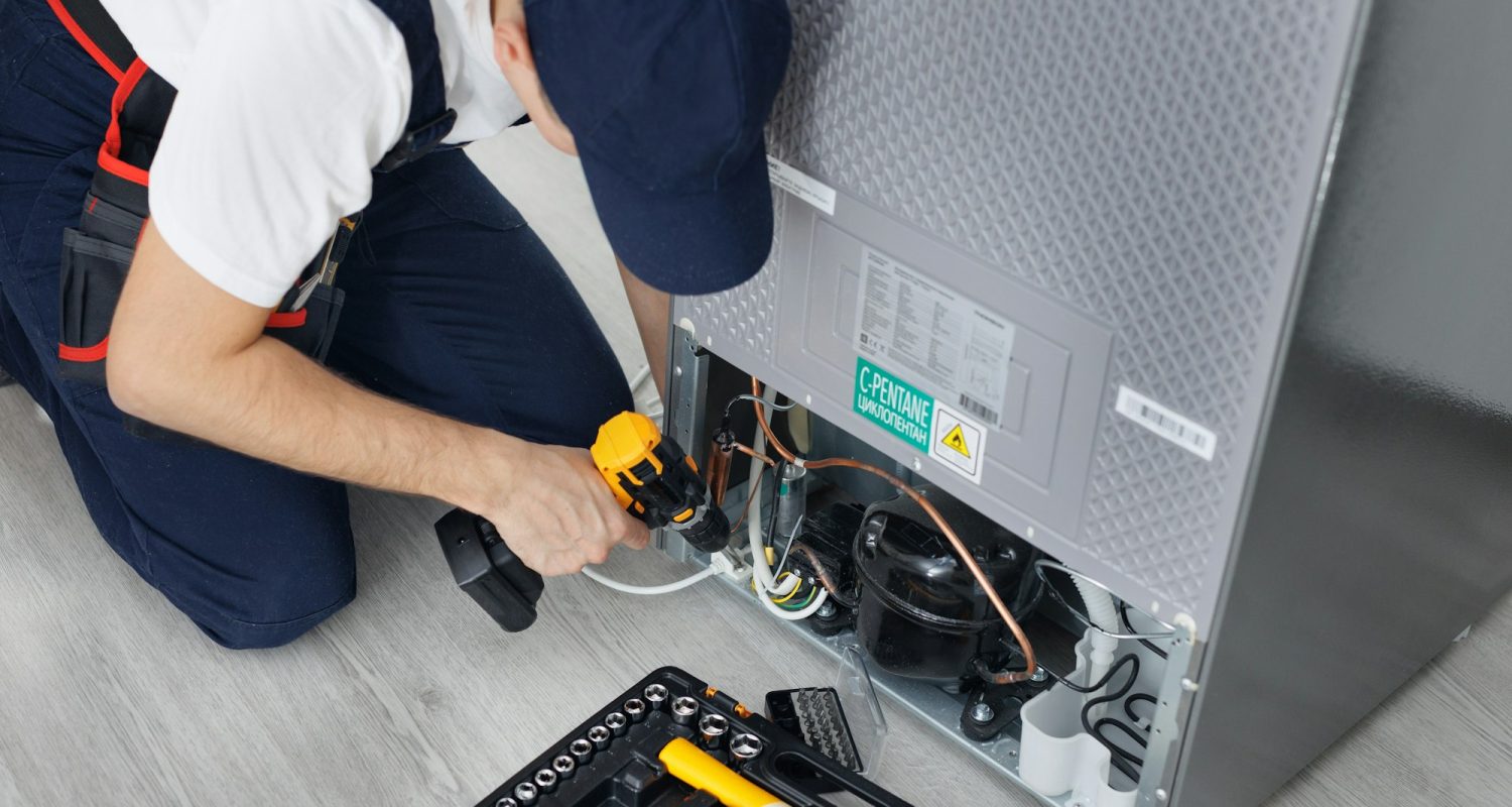 Male technician repairs a refrigerator in the kitchen in close-up.